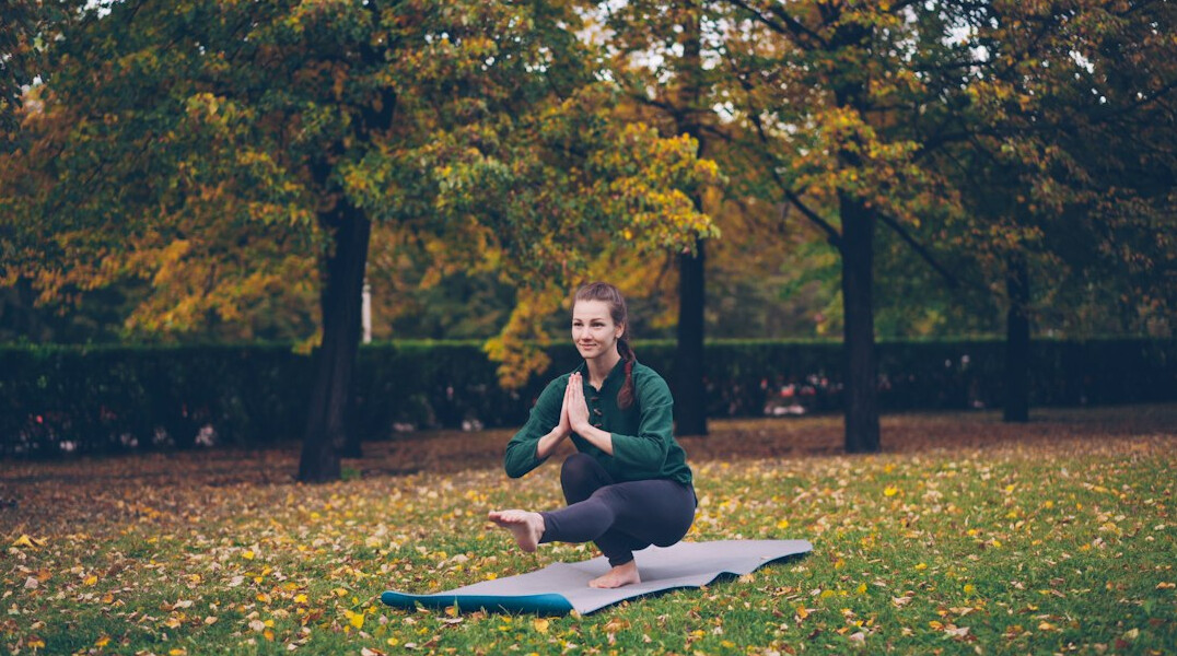 Smiling woman doing yoga outdoors on a mat in the morning